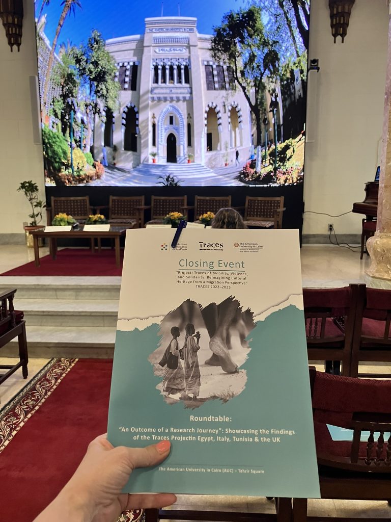 A hand holding a book with the roundtable title and "closing event"